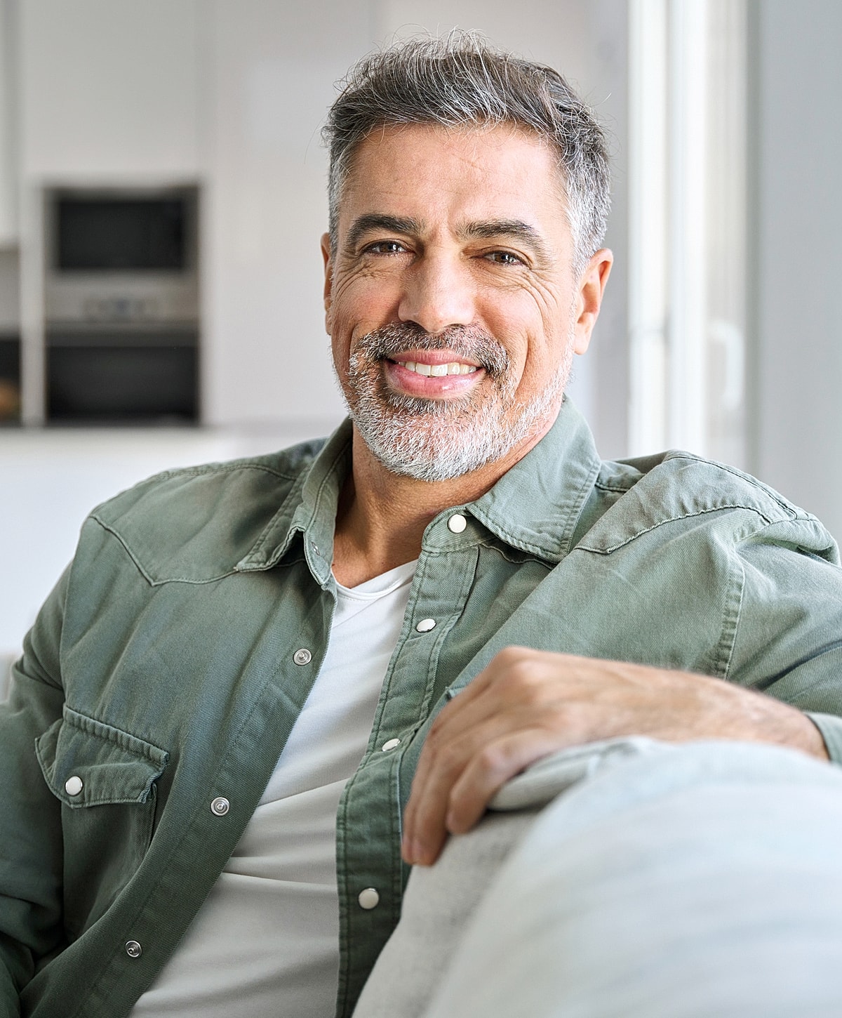 Smiling NYC Incisional Hernia Repair man sitting on a couch indoors.